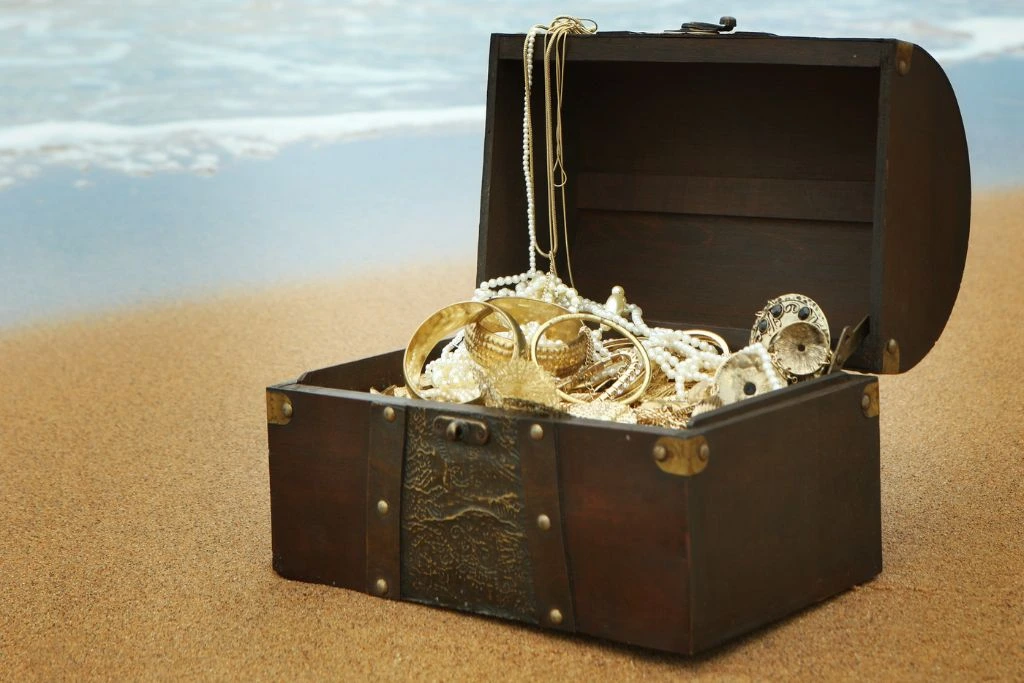 A treasure chest that is full of jewelry on the sand