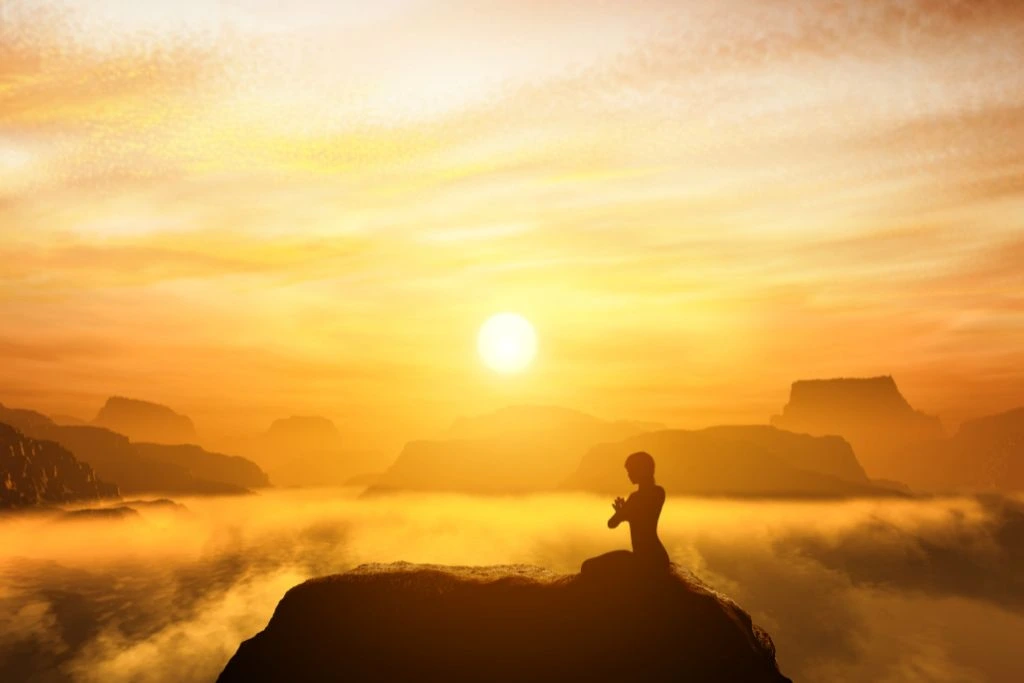 A woman meditating on top of the mountain during sunset