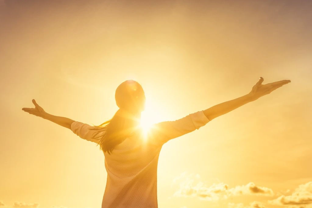 A woman stretching her arms sideways while facing the sun