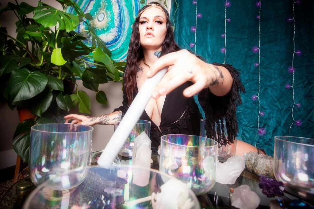 A woman using a singing bowl with different kinds of crystals on the table