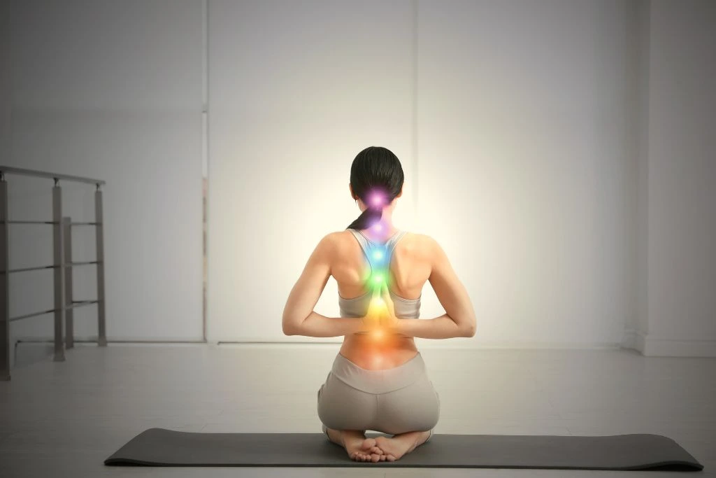 A young woman practicing a yoga pose with different color spots on her back indicating chakra points
