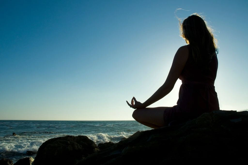 A silhouette of a woman meditating near the beach