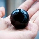 A person holding a round black obsidian crystal