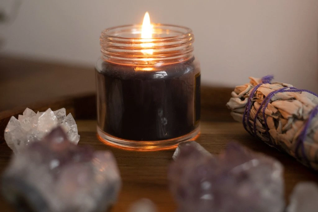 burning candle surrounded by crystals and smudge sticks