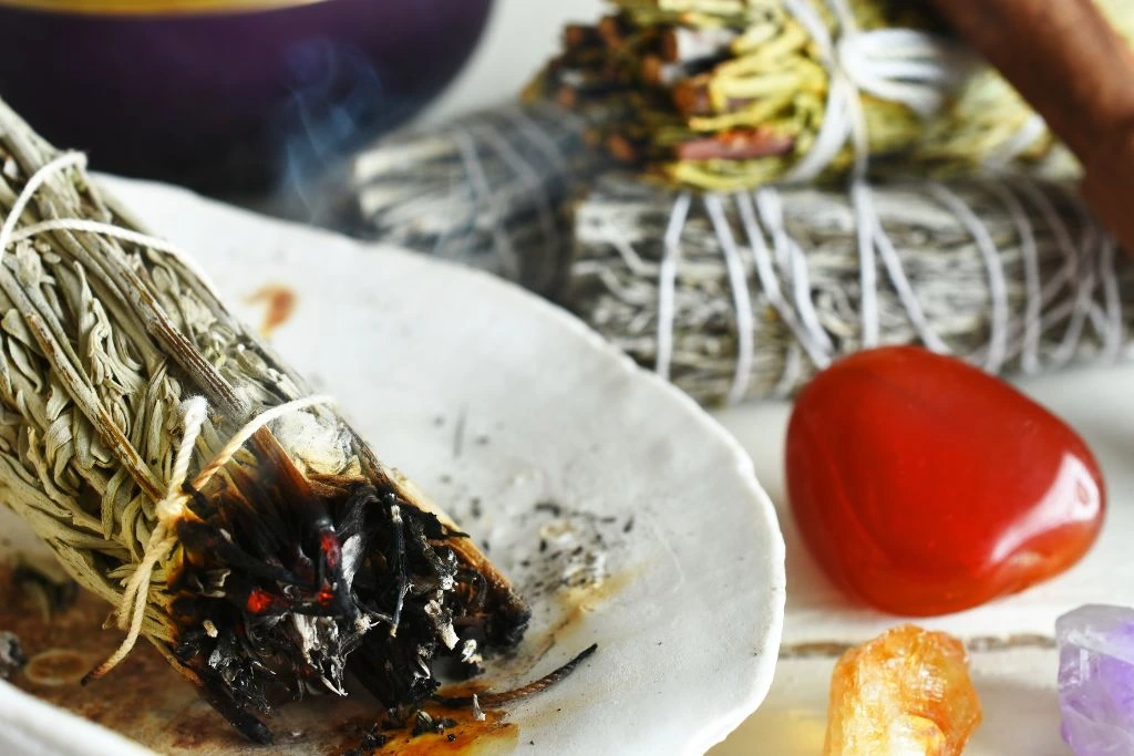 A burning white sage smudge stick and a carnelian crystal on the table