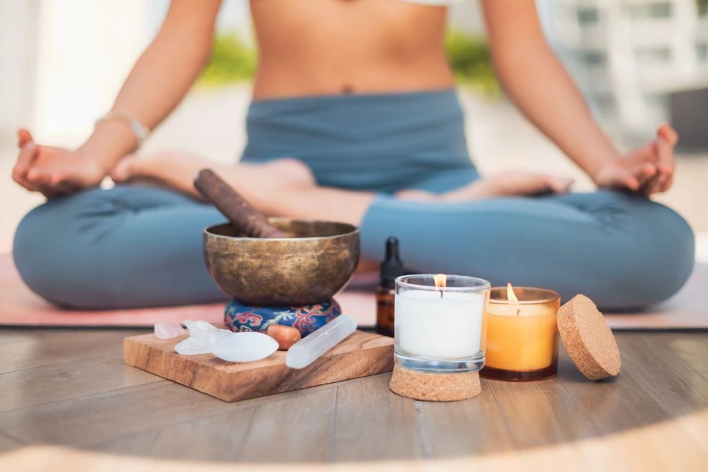 A person is sitting behind the singing bowl with crystals and candles beside it.