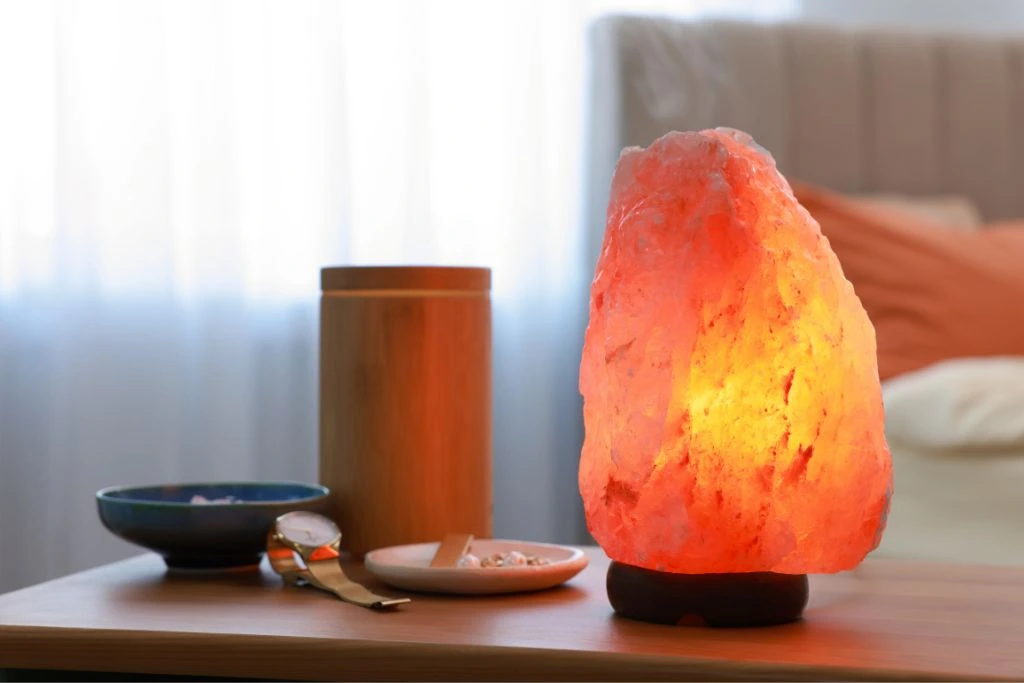 Himalayan Salt lamp placed on a small table beside a bed inside a bedroom
