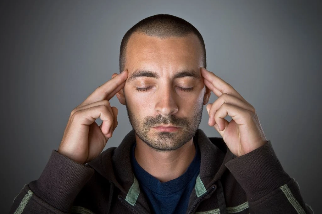 A man close eyes is touching the sides of his head with his two fingers