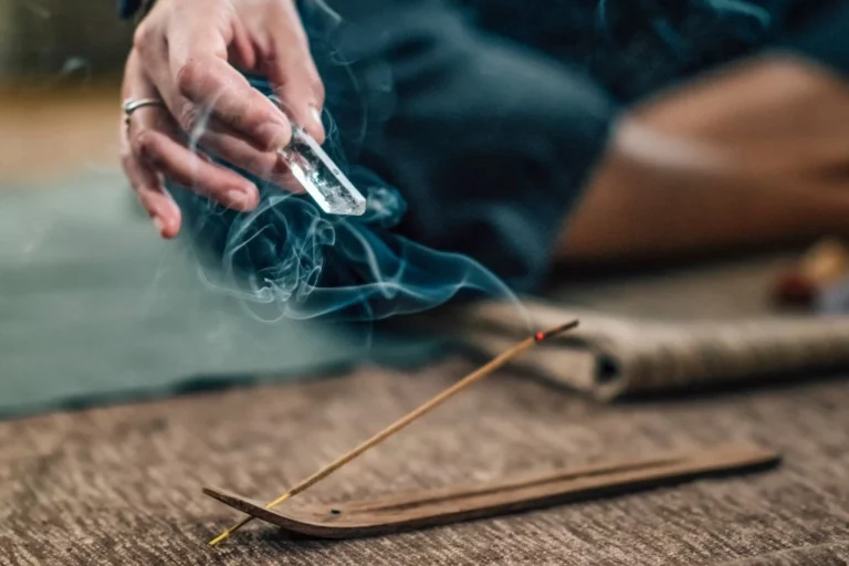 A woman holding a crystal chakra wand while being smoked with incense
