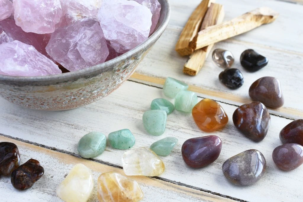 A bowl full of rose quartz crystal and a few different kinds of crystals on the table