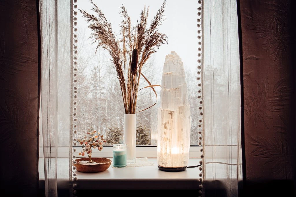 selenite crystal lamp placed near the window right next to small lucky tree decoration