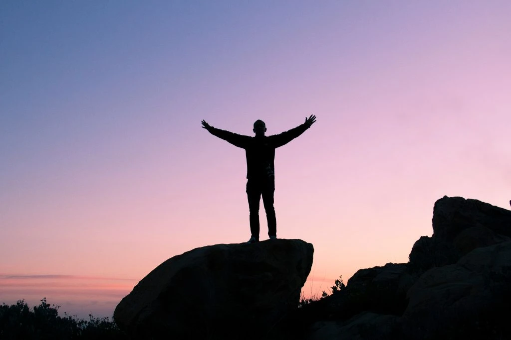 A Silhouette of a person Raising his or her Hands on top of a rock