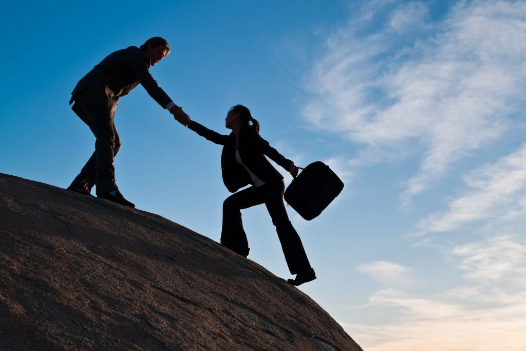 A man helping a woman to get on top of the rock