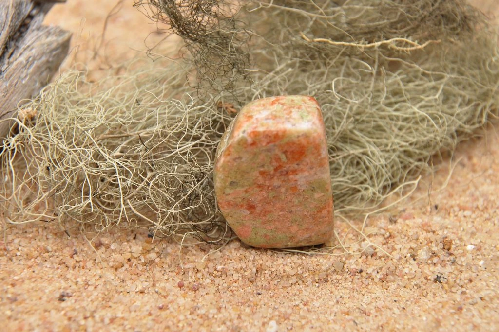A polished Unakite crystal on a sand