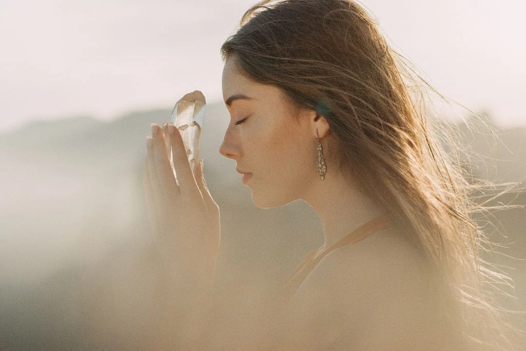 A woman holding a clear quartz crystal near her forehead