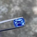 The tweezer is holding a blue topaz on a greyish background