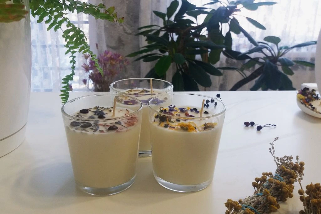 homemade candles with herbs, flowers and crystals on a white table