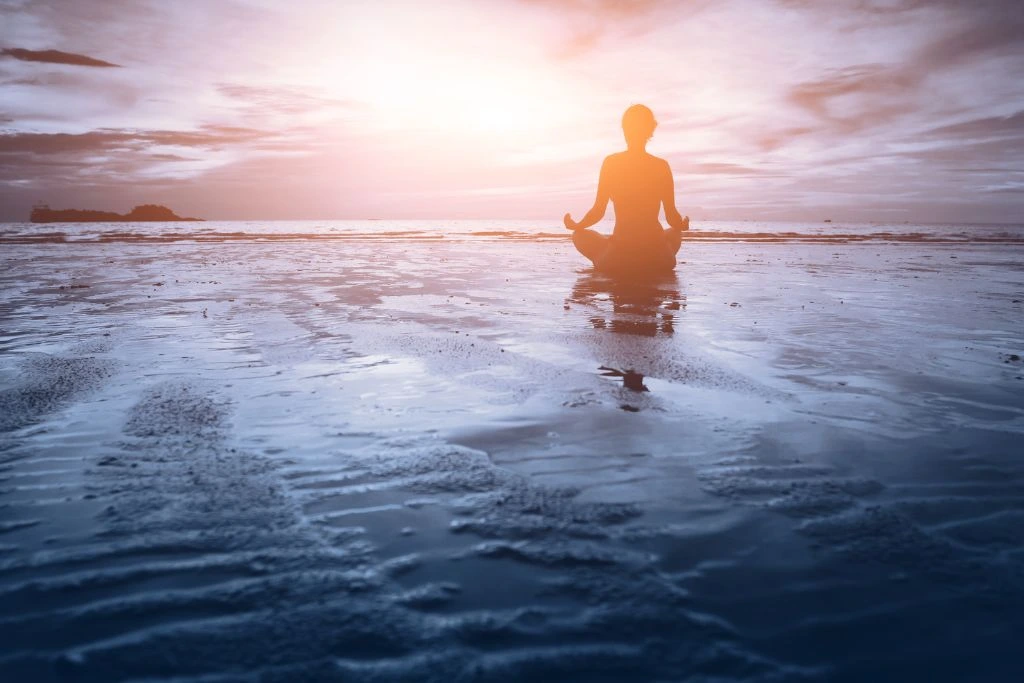 A person sitting on a wet sand near the shore