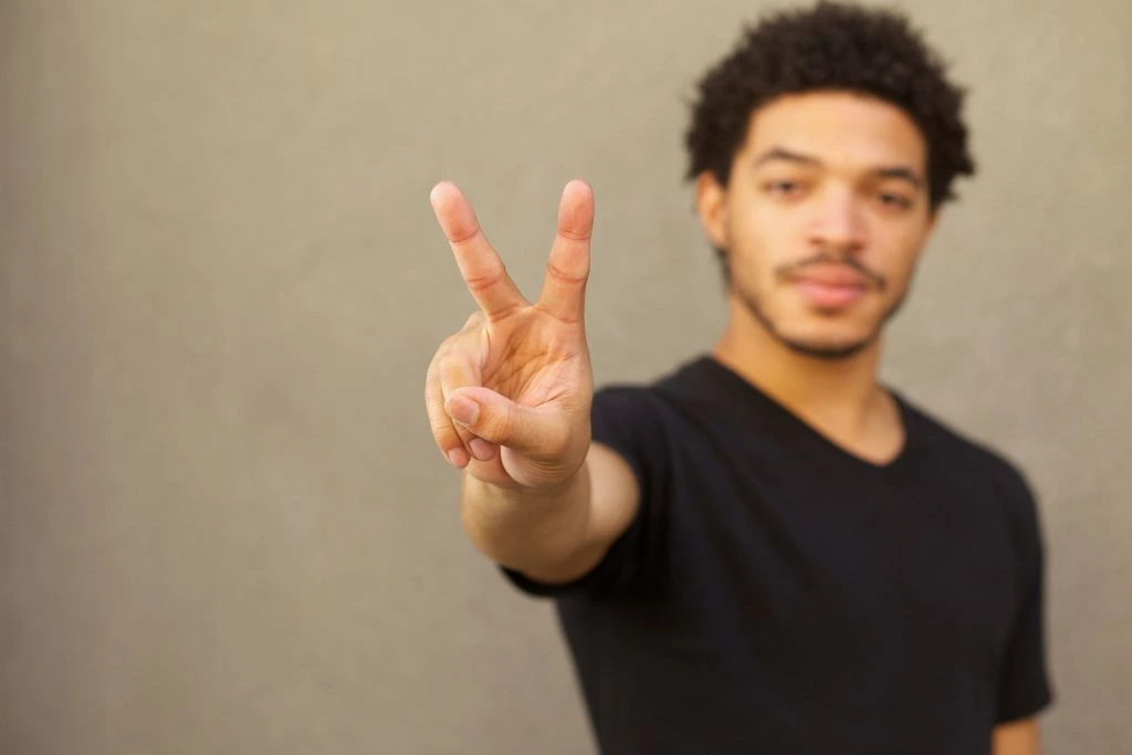 a man standing and showing a peace sign on his hand