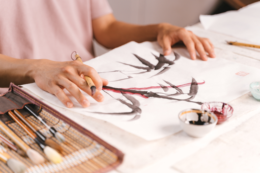 A person drawing a bamboo tree on a white paper using a traditional pen