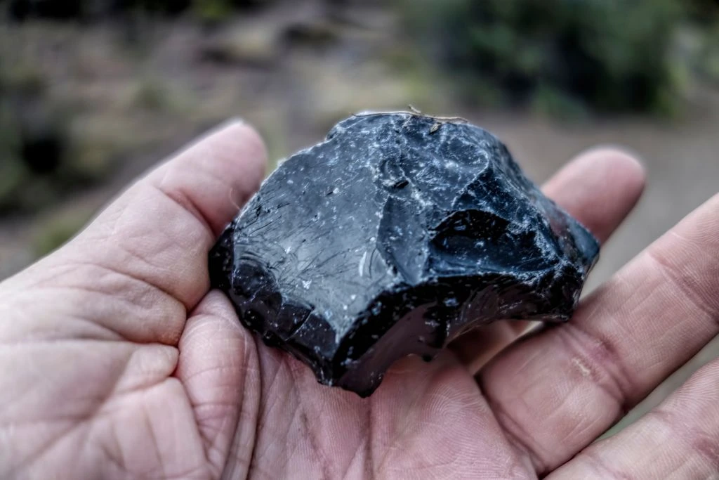 A person holding a raw black obsidian crystal