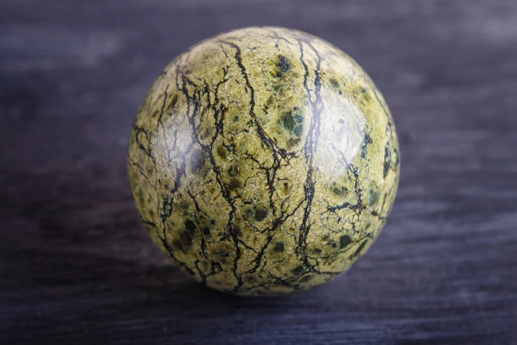 A polished serpentine sphere crystal on a table