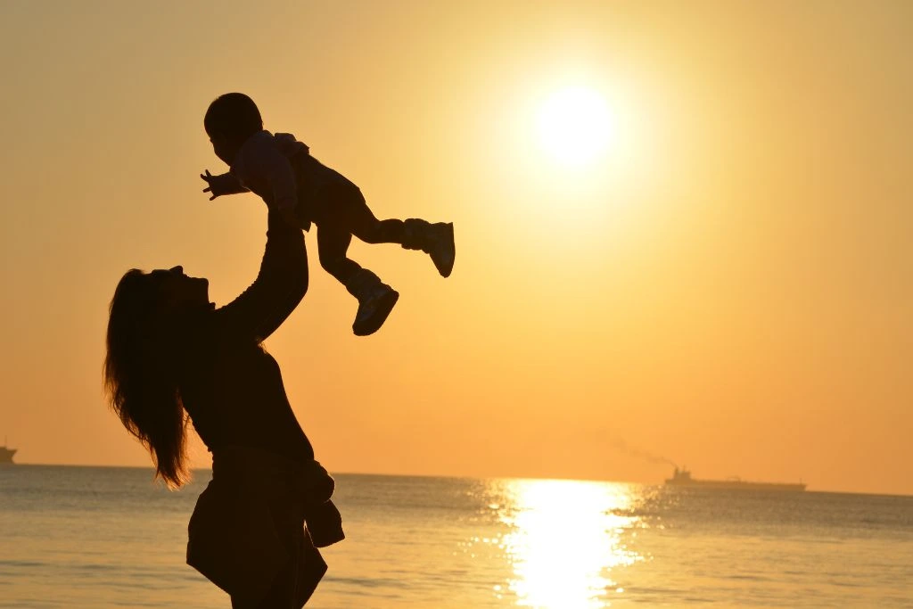 A silhouette of a mother carrying a child with her two hands