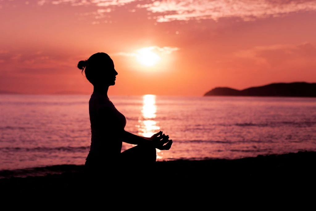 A silhouette of a woman meditating near the shore