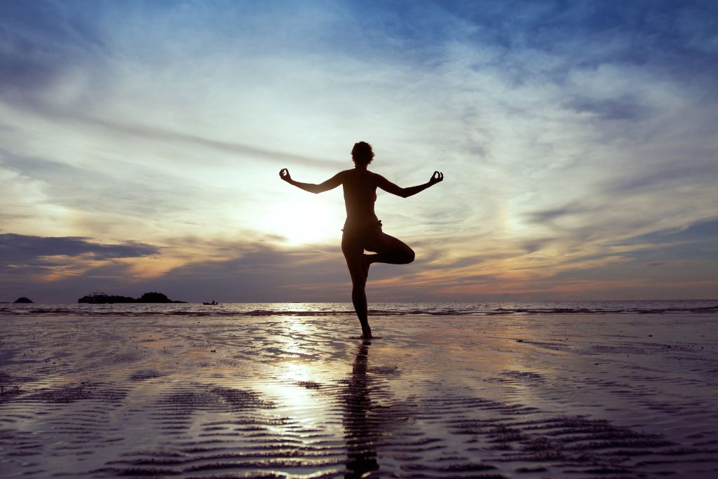 A silhouette of a woman standing on one foot near the shore