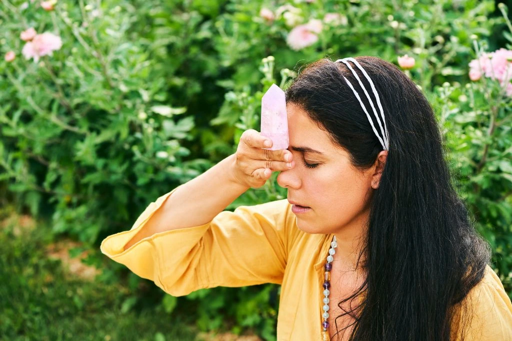 A woman holding a kunzite crystal on her forehead 