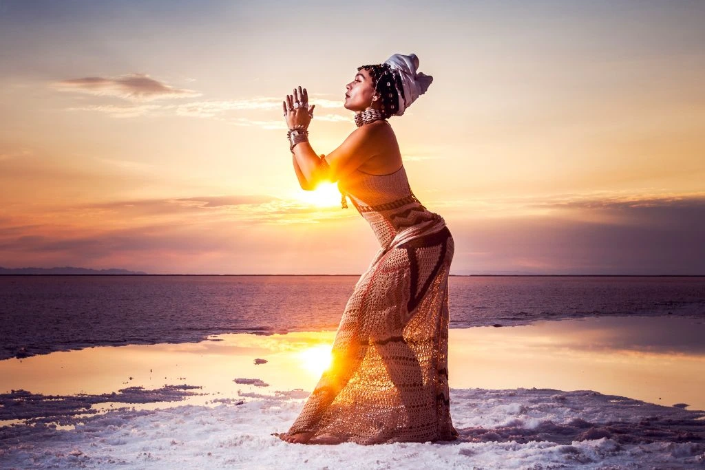 A woman praying while standing on the sand