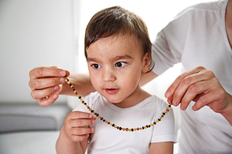 A person putting a baltic ember necklace on a baby boy