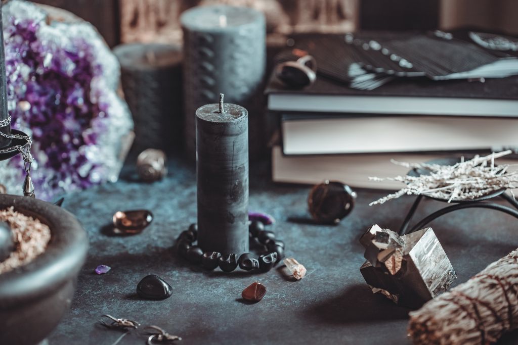 Black candles, sage, books, and crystals on a table with a dark set-up 