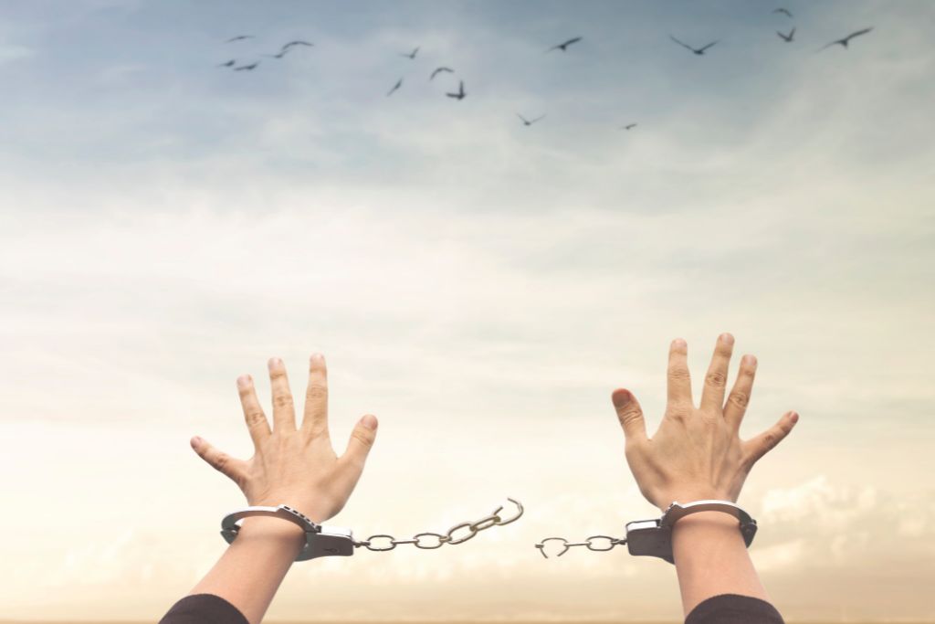 A person's hands reaching the sky with the chains of the handcuffs being broken