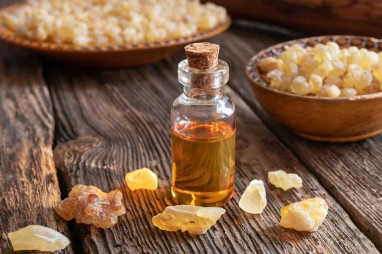 A bottle of essential oil beside crystals and crystals in a bowl on a wooden set