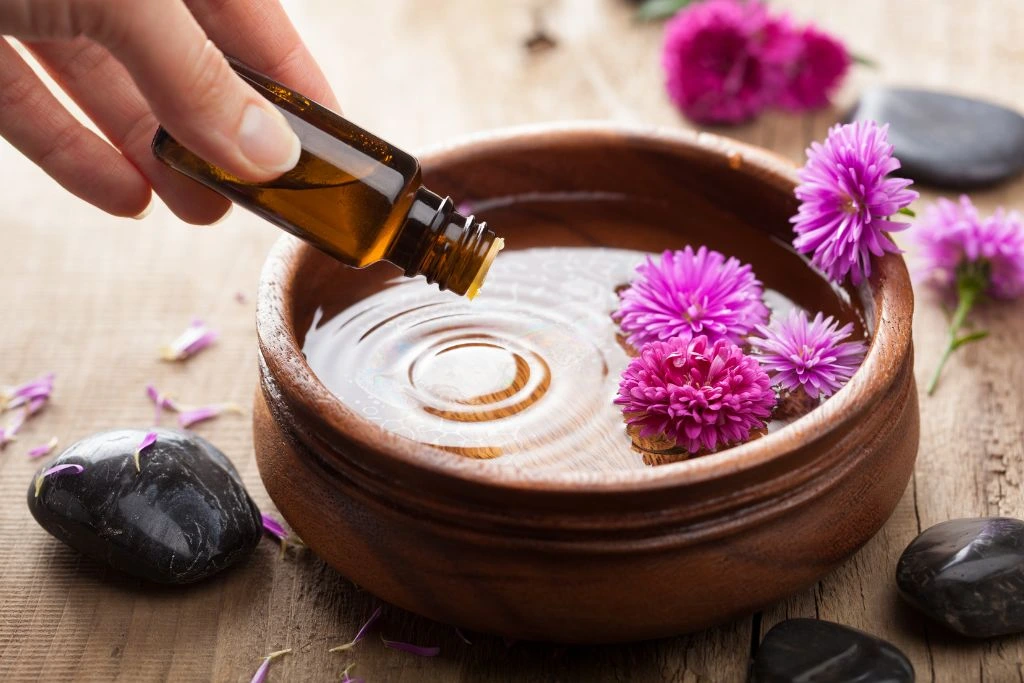 A person adding some essential oils on a bowl with flowers