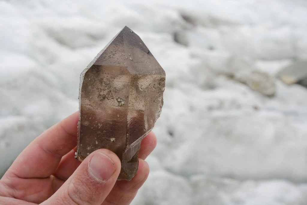 hand holding a smoky quartz crystal on a snow background