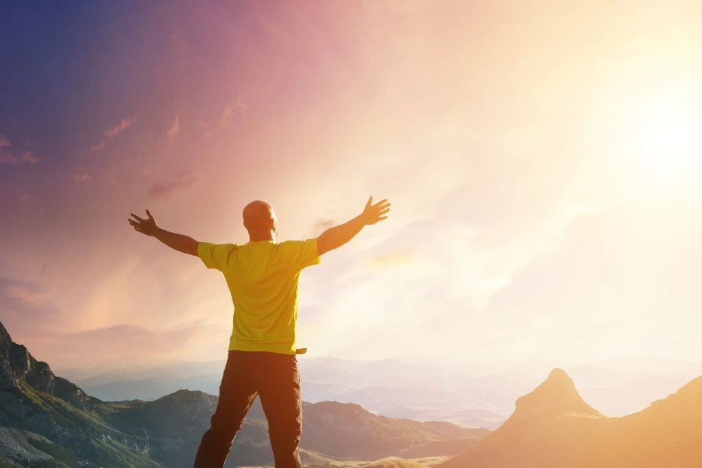 Man with outstretched arms on top of a mountain overlooking the sky, ocean and mountains