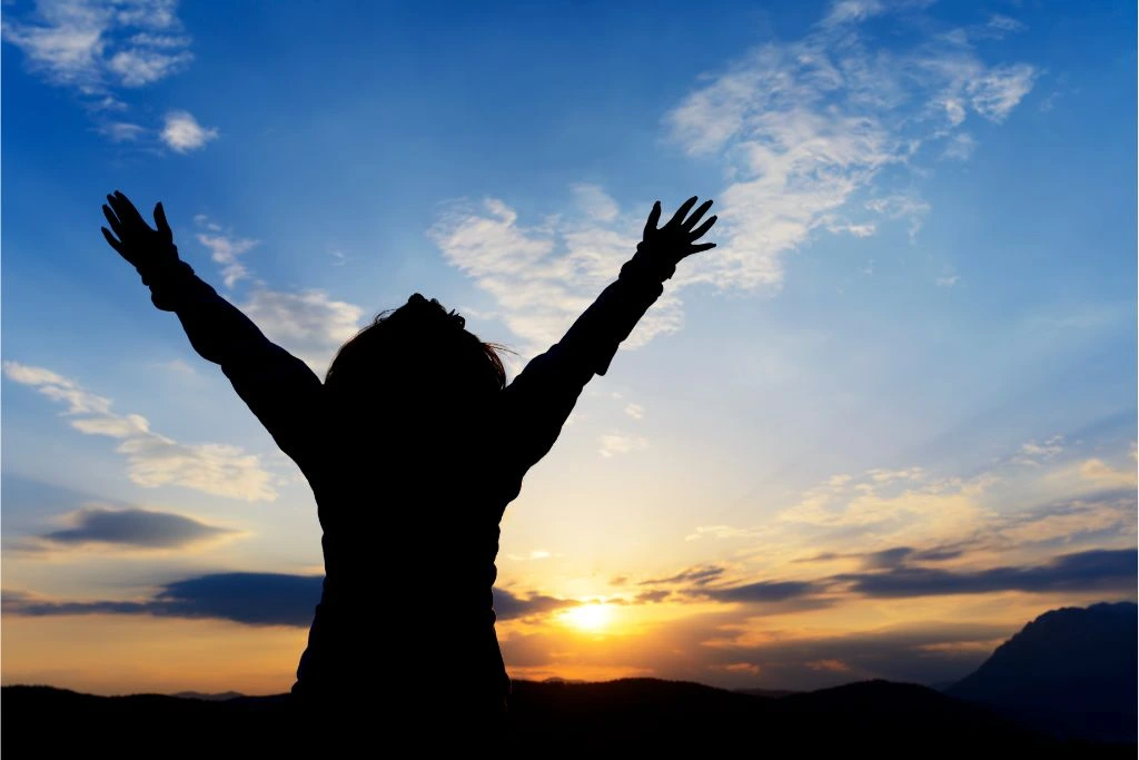 Silhouette of outstretched arms of a person on a sunrise background 