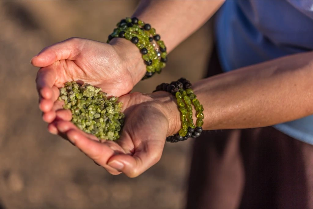 Person wearing crystal bracelets holding numerous peridot stones