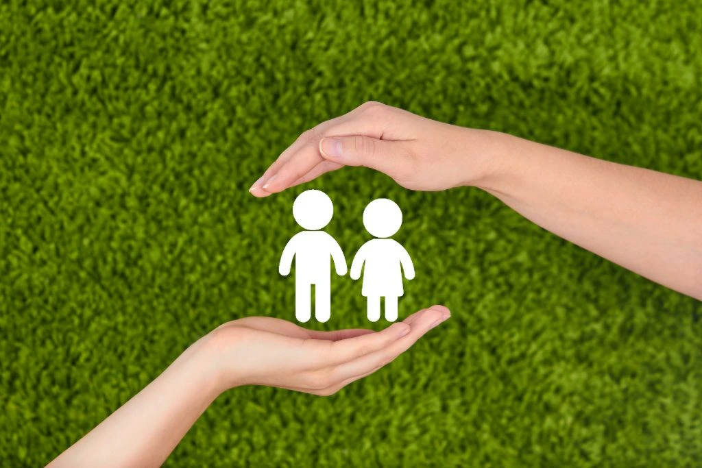 Hands protecting a paper cut people on a green grass background