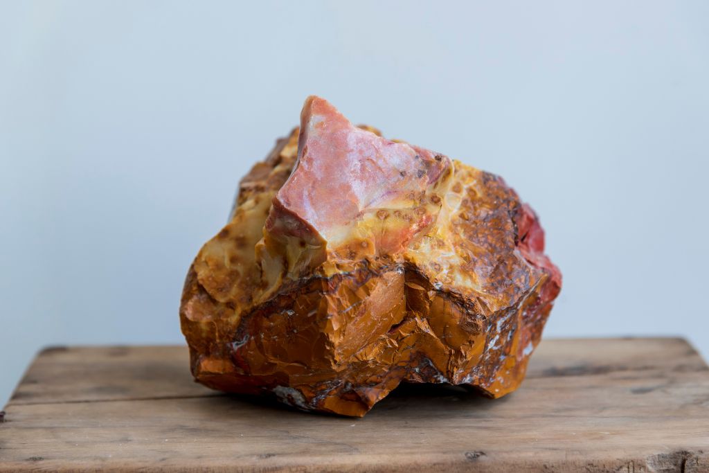 Raw orange gemstone on top of a wooden board on a white background
