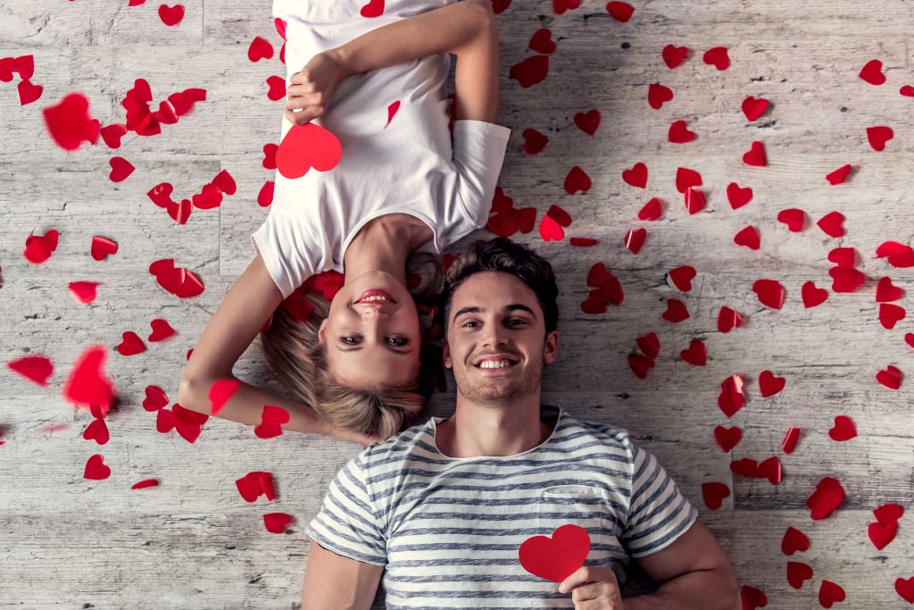 Romantic young couple laying on the floor with paper hearts