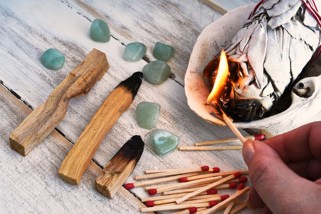A picture of sage, crystals, and a lit match stick
