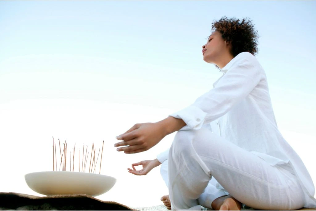 Woman meditating with incense with the sky as its background