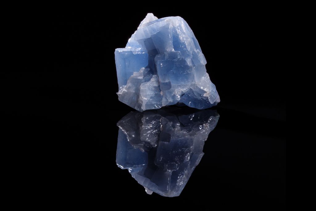 A blue calcite crystal on a black reflective background