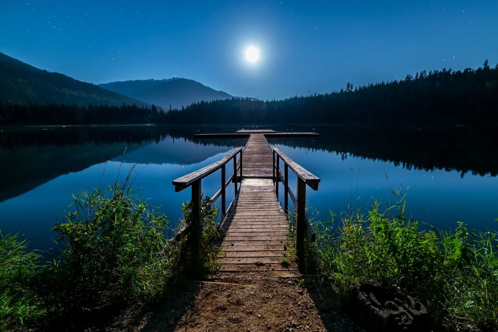 The moonlight shines over the dock in the lake