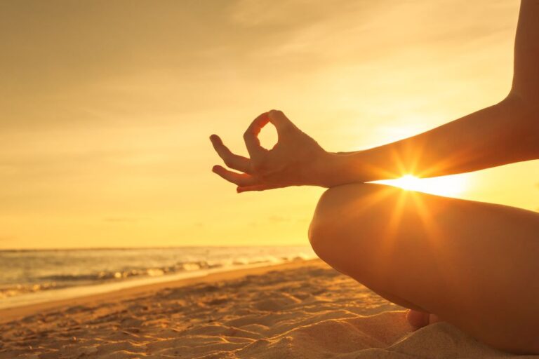 A person meditating by the ocean bay with the sun setting