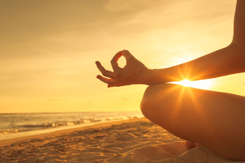 A person meditating by the ocean bay with the sun setting 