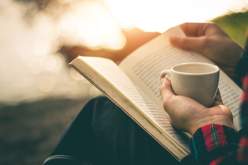 A person is reading a book while holding a teacup
